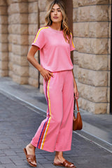 Woman wearing a pink outfit with colorful stripes standing against a stone wall.