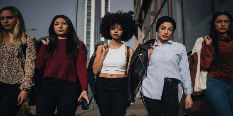 Five women standing together outdoors with a cityscape background