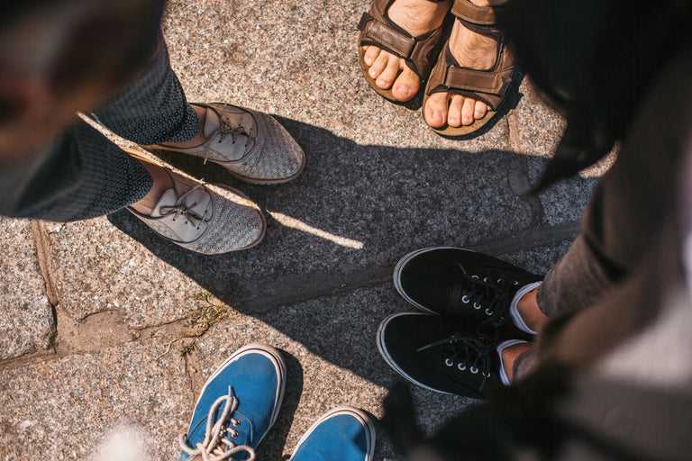 Close-up of feet wearing different types of shoes on a pavement.