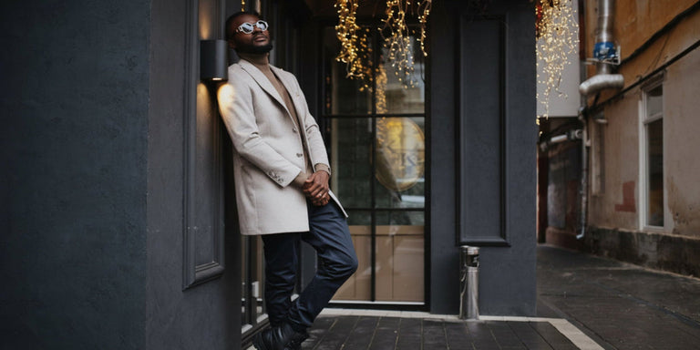 Man in a beige coat standing against a building entrance with decorative lights.